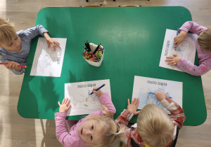 Dzieci wykonują pracę plastyczną przy stoliku