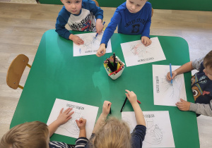 Dzieci wykonują pracę plastyczną przy stoliku