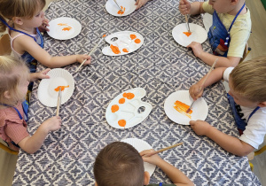 Dzieci kolorują papierowe talerzyki na pomarańczowo