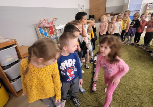 Dzieci stoją w rzędzie, ustawiają kolejno buty