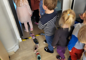 Dzieci stoją w rzędzie, ustawiają kolejno buty