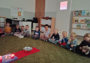 Dzieci siedzą w kole dookoła świeczek i czekają na rozpoczęcie wróżb