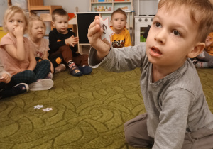 Dzieci siedzą w kole, chłopiec pokazuje wylosowany numer