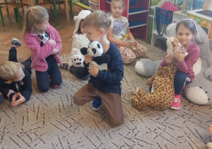 Dzieci siedzą na dywanie z maskotkami