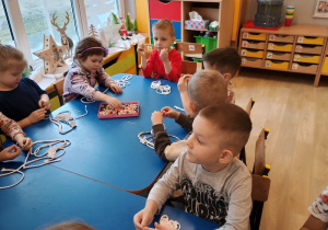 dzieci nawlekają z pomocą patyczka korale dla babci
