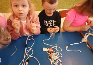 dzieci nawlekają z pomocą patyczka korale dla babci