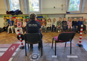 Dzieci siedzące na ławce słuchają strażniczki miejskiej