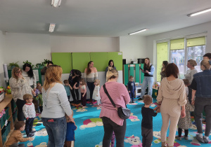 Rodzice z dziećmi stoją w kole na dywanie