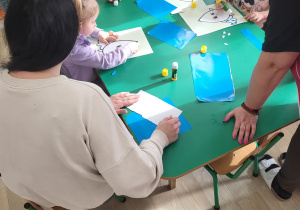 Dzieci z rodzicami wykonują pracę plastyczną przy stolikach