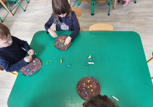 Dzieci przy stolikach wyklejają papierowe pączki plasteliną