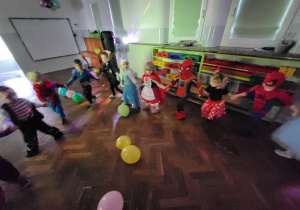 Dzieci w przebraniach tańczą w kole, trzymając się za ręce