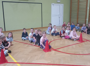 Dzieci siedzą w rzędach na sali gimnastycznej