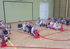 Dzieci siedzą w rzędach na sali gimnastycznej