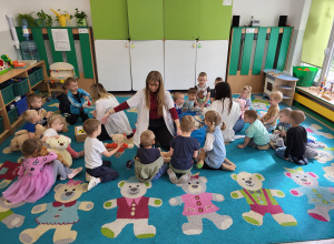 Dzieci siedzą na dywanie i słuchają studentek