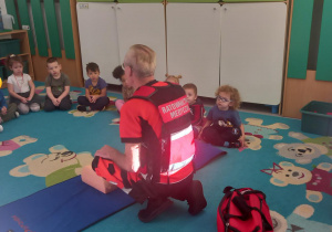 Dzieci siedzą w kole słuchając ratownika