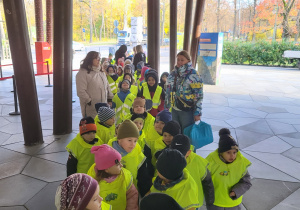 Dzieci ubrane w kamizelki odblaskowe czekają na wejście do zoo