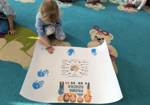 Dziewczynka tworzy niebieski odcisk swojej dłoni na plakacie