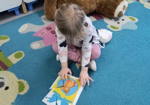 Dziewczynka układa ilustracje przedstawiającą prezent z ukrytym w środku misiem