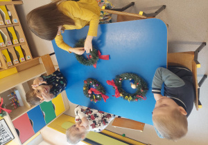 Dzieci przywiązują wstążeczki, nakładają lampki i bombki