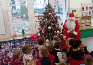 Dzieci siedzą przy choince z Mikołajem