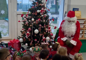 Dzieci siedzą przy choince z Mikołajem