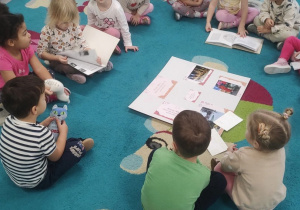 Dzieci siedzą na dywanie, oglądają książki
