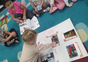 Dzieci siedzą na dywanie, oglądają książki oraz mapę ze zdjęciami