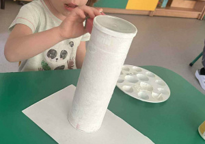 Dziewczynka maluje kartonową rolkę na biało