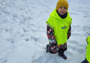 Chłopiec idzie po śniegu i uśmiecha się