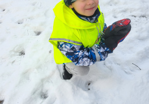 Chłopiec kuca i lepi kulkę ze śniegu