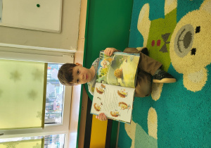 Chłopiec siedzi i trzyma w dłoniach otwartą książkę, prezentując jej strony