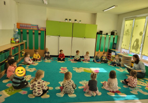 Dzieci siedzą w kole uważnie wsłuchując się w tekst czytany przez prowadzącą