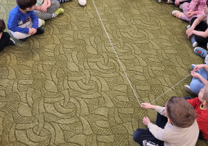 Dzieci siedzą w kole, podają sobie włóczkę