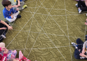 Dzieci siedzą w kole, trzymają w rękach włóczkę