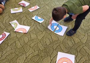 Dzieci siedzą w kole, chłopiec łączy połowy pączków