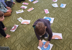 Dzieci siedzą w kole, chłopiec łączy połowy pączków