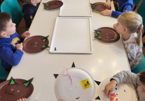 Dzieci siedzą przy stoliku z papierowymi talerzykami