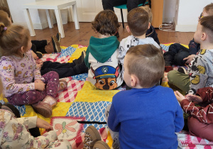 Dzieci siedzą na kocach i słuchają prowadzącej