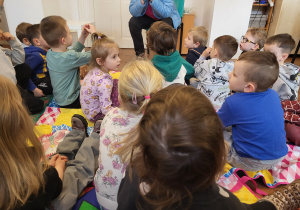 Dzieci siedzą na kocach i słuchają prowadzącej
