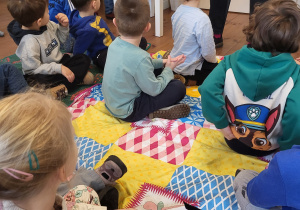 Dzieci siedzą na kocach i słuchają wiersza