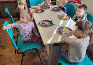 Dzieci siedzą przy stolikach i czekają na dalsze instrukcje