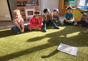 Dzieci w opaskach siedzą na dywanie