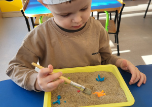 Chłopiec pędzelkiem odkopuje dinozaury z piasku