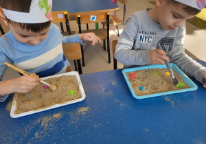 Chłopcy pędzelkiem odkopują dinozaury z piasku