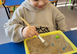 Chłopiec pędzelkiem odkopuje dinozaury z piasku