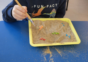 Chłopiec pędzelkiem odkopuje dinozaury z piasku