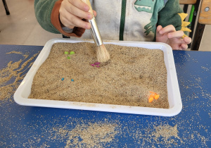 Chłopiec pędzelkiem odkopuje dinozaury z piasku