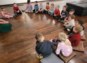 Dzieci siedzą na poduszkach w półkolu