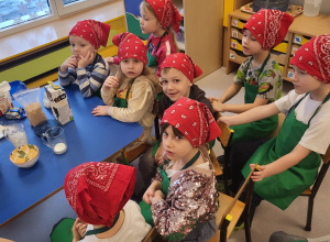 Dzieci w chustkach i fartuszkach siedzą obok stolików
