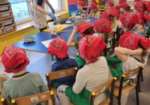 Dzieci siedzą przy stoliku i obserwują pracę prowadzącej warsztaty